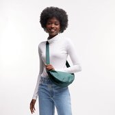 Een vrouw met afro haar, gekleed in een witte coltrui en jeans, draagt een smaragdgroene crossbodytas.