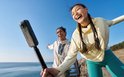Twee lachende mensen, een man en een vrouw, met Insta360 X5 op een heuveltop bij zee.
