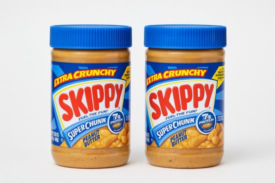 Twee potten Skippy Super Chunk pindakaas extra crunchy met blauwe deksels. Het etiket is blauw met een gele en rode rand. 'Skippy', 'Extra Crunchy' en 'Super Chunk' zijn duidelijk zichtbaar.