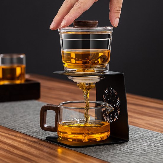 Gouden thee druppelt van glazen theezetter met houten deksel naar glazen schenkkan met houten handvat.