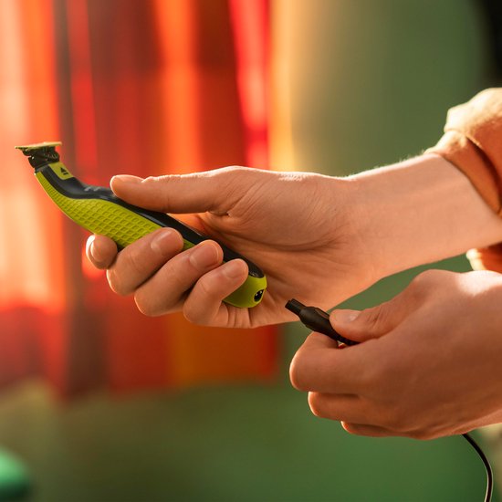 Hand houdt gele en zwarte OneBlade trimmer bij USB-A oplaadkabel.