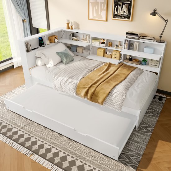 Wit slaapbank met uitschuifbaar bed en hoofdeinde met opbergvakken, boeken, telefoon en decoraties.