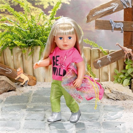 Meisje met blond haar draagt roze shirt met 'BE WILD' tekst en een konijn, groene broek, zilveren laarsjes en draagt een roze tas met print.