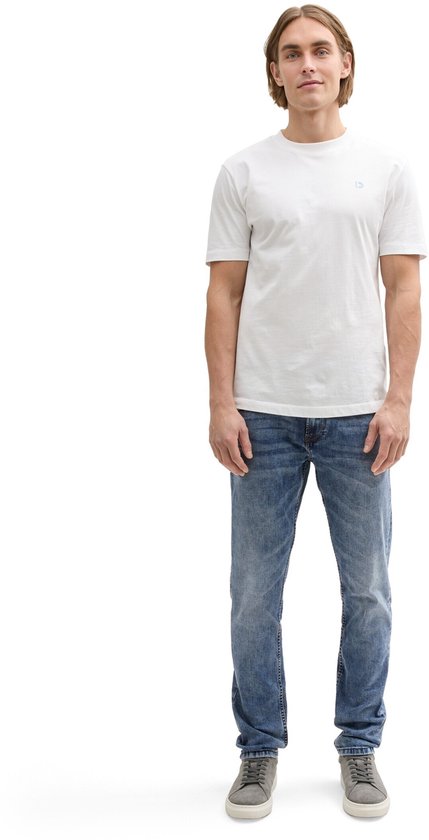 Man in wit T-shirt met logo, en slanke, lichtblauwe spijkerbroek.