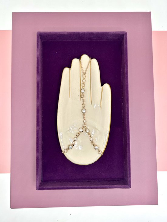 Gouden handketting met parels op witte handvormige display.