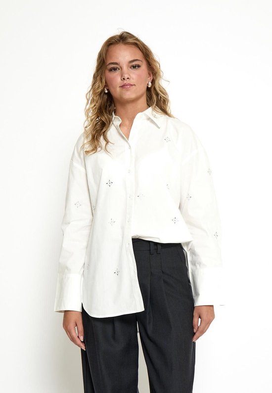Model draagt een witte oversized blouse met parelmoer knopen en geborduurde sterren.