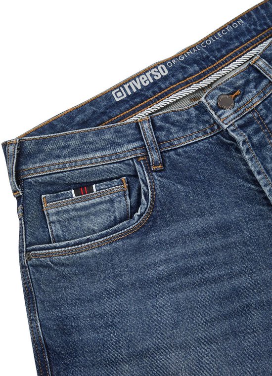 Detail van de voorkant van een blauwe jeans met zakken, label 'riverso ORIGINAL COLLECTION'.