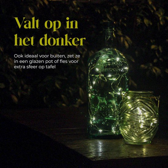 Een groen glazen fles en pot, gevuld met warm witte lichtsnoeren, op een donkere tafel.