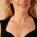 Model met blond haar draagt een gouden hartvormige hanger met de letter M aan een ketting en een zwarte top.