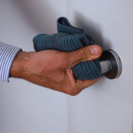 Une main avec un chiffon en microfibre bleu-gris nettoie une poignée de porte.