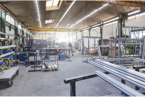 Atelier avec structures métalliques, outils et une grue au plafond.