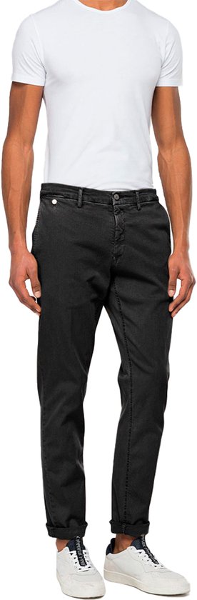 Man in witte T-shirt en donkergrijze jeans, met opgerolde broekspijpen.