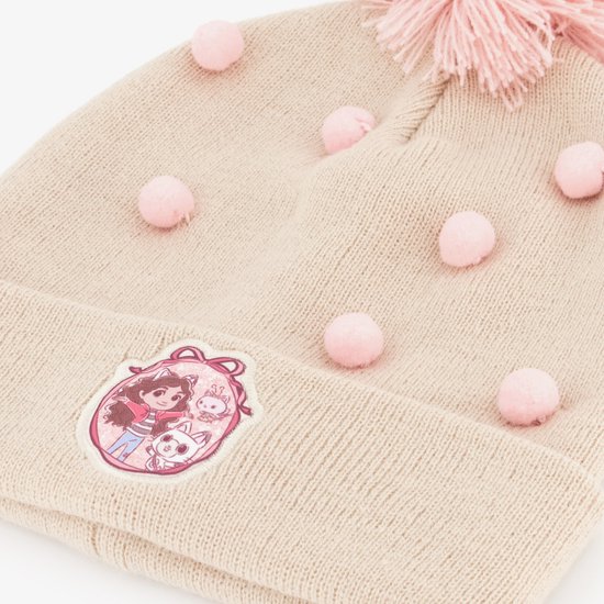 Detail van beige gebreide muts met roze pompon en stippen, met patch van Gabby en kat.