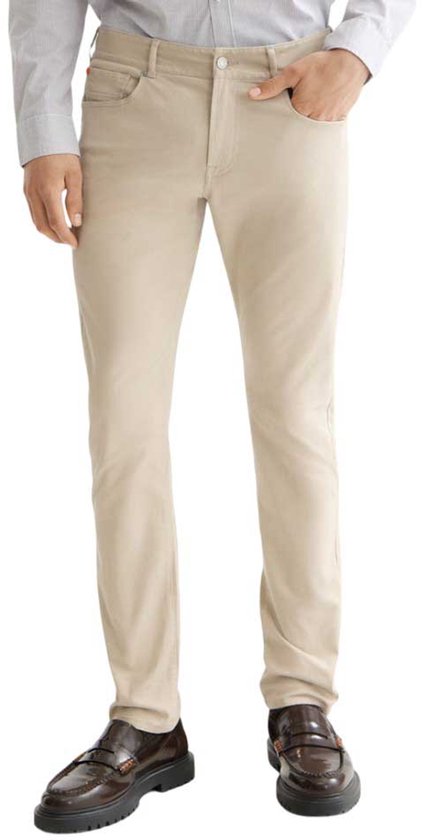 Model draagt een beige broek, gecombineerd met een licht overhemd en donkere schoenen.