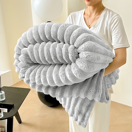 Iemand houdt een opgevouwen, lichtgrijze, geribbelde fleece deken vast met een zachte textuur.
