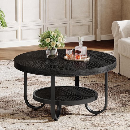 Zwarte ronde salontafel met een plank eronder, met een vaas bloemen, twee glazen en een karaf op een dienblad.