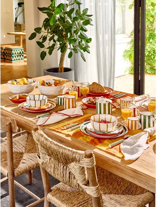 Gedekte tafel met servies in geel en groen gestreept, op een houten tafel met stoelen.