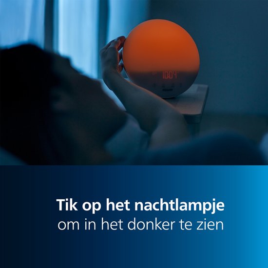 Een vrouw in bed met gesloten ogen, terwijl de Philips wek-up light diep oranje oplicht en 10:04 weergeeft.