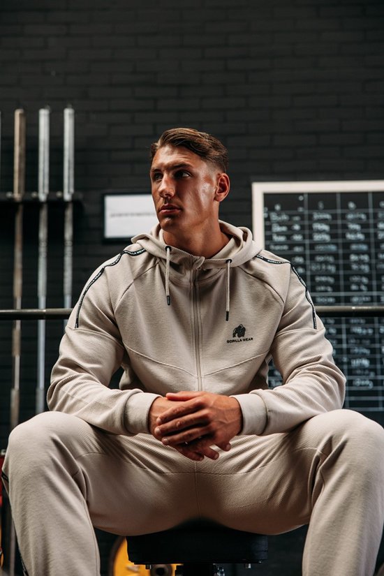 Man zittend met beige Gorilla Wear trainingsjack in de sportschool.