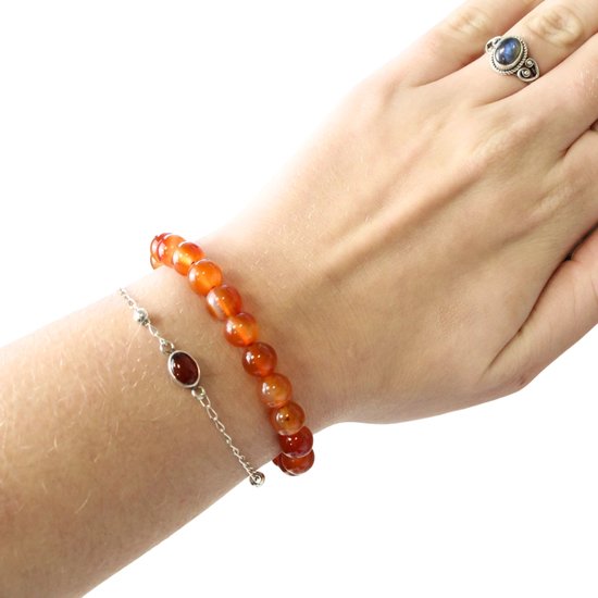 Hand met een armband van oranje carneool kralen en een zilveren armband met rode steen.