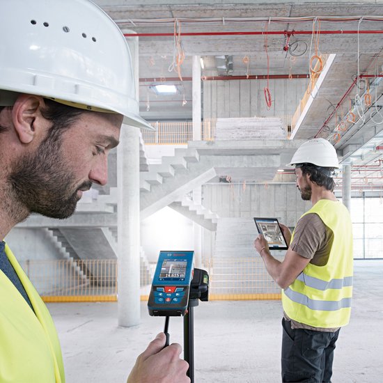 Twee bouwvakkers met helmen en hesjes, één met een Bosch laser afstandsmeter, de ander met een tablet.