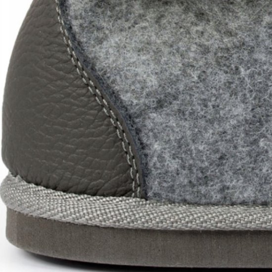 Detail van de hiel van een grijze vilten slof met donkergrijs leer en stiksels.