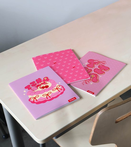 Drie Tina schriften op een bureau. Een schrift met strikjes, een met tekst 'Tina' en een met een taart met kersen.