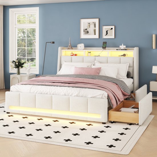 Een wit gestoffeerd bed met een hoofdbord met opbergvakken, LED-verlichting en lades. Het bed is opgemaakt met wit beddengoed, een roze plaid en een zwart-wit geblokte plaid.