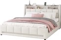 Wit gestoffeerd bed met hoofdbord met opbergvakken, opgemaakt met wit beddengoed, roze plaid en zwart-wit geblokte plaid.