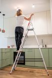 Vrouw wisselt een lamp op de aluminium huishoudladder, keukeninterieur.