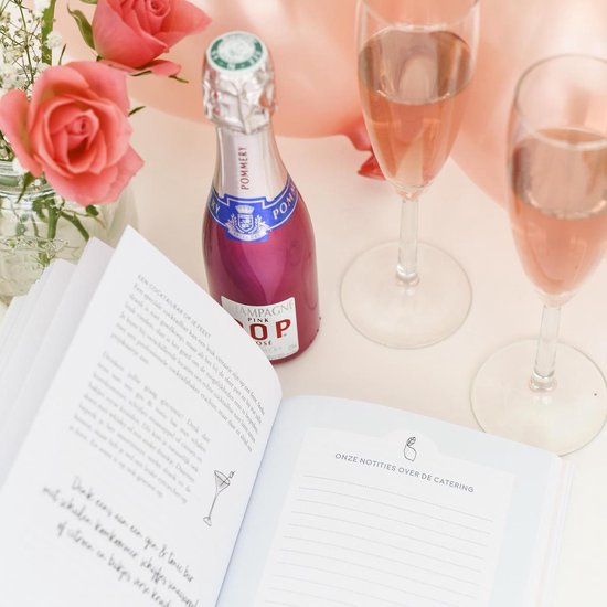 Een open boek met de tekst 'Trouwen doe je zo!' ernaast een flesje Pommery Pink Pop champagne, roze rozen en twee glazen champagne.