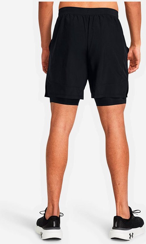 Man in zwarte sportbroek met reflecterende Under Armour logo's op de achterkant van de broekspijpen.