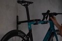 Zwarte racefiets met blauw frame hangt aan zwarte fietsmuurbeugel, een hand past het aan.