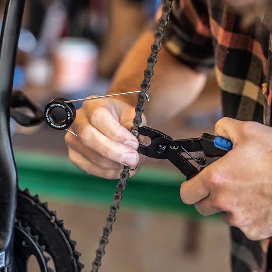 Mains assemblant une chaîne de vélo avec une pince à chaîne noire aux poignées bleues.