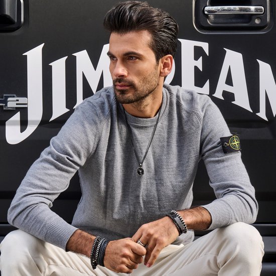 Man met grijze trui, witte broek, zilverkleurige ring en meerdere armbanden.