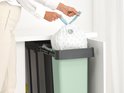 Een hand die een vuilniszak met hengsels uit een mintgroene Brabantia prullenbak haalt.