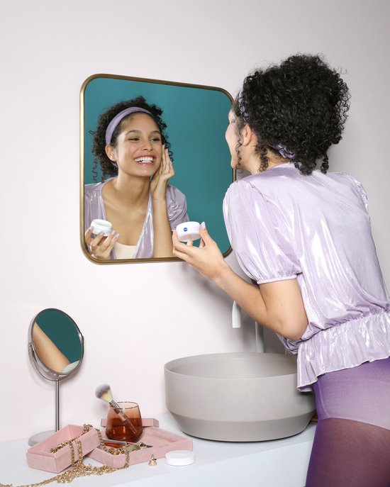 Vrouw met krullen brengt Nivea Q10 Energy crème aan voor een spiegel.