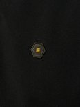 Detail van een zwart poloshirt met een zeshoekig logo met gele strepen.