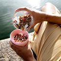 Een vrouw met een gele jurk voegt muesli toe aan een roze Mepal lunchpot.
