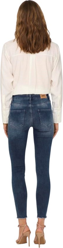 Vrouw in witte blouse en donkerblauwe skinny jeans met rafels aan de onderkant.