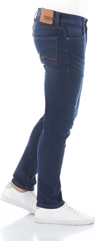 Donkerblauwe tapered fit jeans met oranje stiksels. Een model in een witte sneaker.