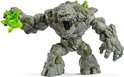 Grijs steenmonster met groene kristallen en mos, grijpend met linkerhand.