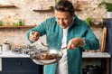 Jamie Oliver lepelend jus over vlees in een RVS koekenpan.