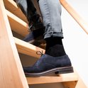 Man in zwarte sokken en donkerblauwe suède schoenen, lopend op een houten trap.