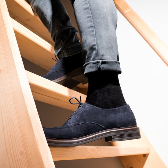 Man in zwarte sokken en donkerblauwe suède schoenen, lopend op een houten trap.
