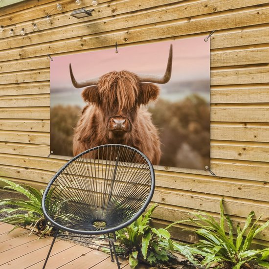 Un Highland coiffé de longues cornes courbées, accroché à une clôture en bois à côté d'une chaise noire.