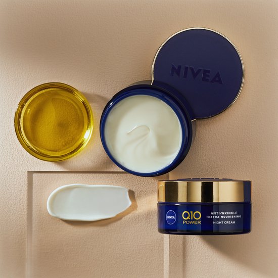 Nivea Q10 nachtcrème met een open potje, schepje crème en een druppel olie naast een gesloten potje.