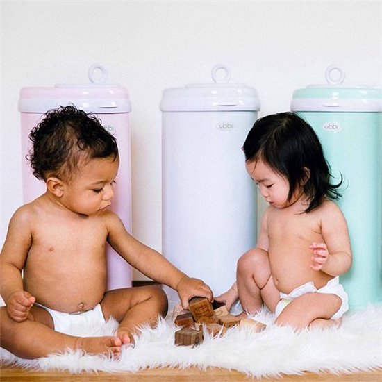 Twee baby's die bij roze, witte en mintgroene Ubbi luieremmers spelen op een wit tapijt.