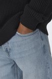 Close-up van een man die zijn hand in de zak van een lichtblauwe jeans steekt.