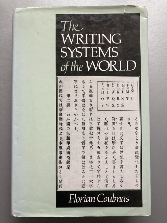 Boek "The Writing Systems of the World" door Florian Coulmas, met op de voorkant tekst in het Engels en Japanse karakters, en een alfabet.